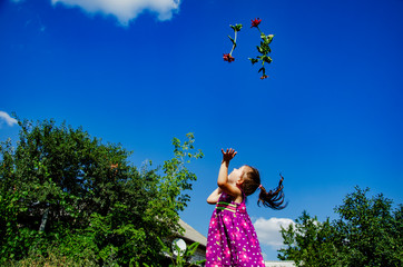 Happy child throws flowers up against the blue sky. A little girl in a beautiful dress is spinning in a summer meadow. Portrait photo of a happy child with flowers. The child runs across the lawn. Chi