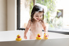 Smiling Toddler Girl Playing With Rubber Ducks In Bathtub
