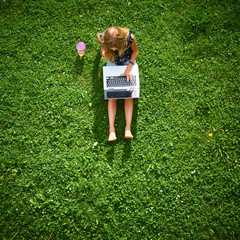 Wall Mural - Child blond girl working on laptop. Playing games or watching movie. View from above
