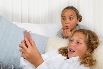 Two preteen, tween, mixed race girls are surprised using a smart phone