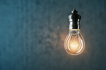Wall Mural - Glowing light bulb on gray wall background.