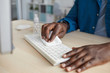 © Seventyfour - Close up of young African-American man wiping keyboard with sanitizing wipes while working at desk in post pandemic office, copy space