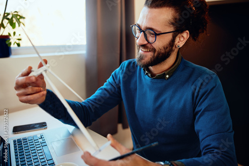 Young attractive bearded innovative hipster sitting in his home office and holding windmill model during corona virus. Sustainable development concept.