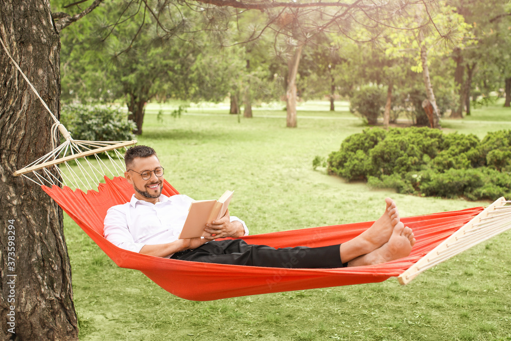 Handsome businessman reading book while relaxing in hammock outdoors