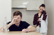 © Olha - Drinking problem drunk man in a young family. A man drinks while sitting at a table in the kitchen, an upset woman stands next to a man and looks at him