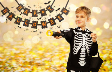 Poster - halloween, holiday and childhood concept - happy boy in black costume of skeleton with bucket of candies and flashlight trick-or-treating over garland string decoration and lights on background