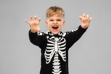 Poster - halloween, holiday and childhood concept - boy in black costume with skeleton bones making spooky faces over grey background