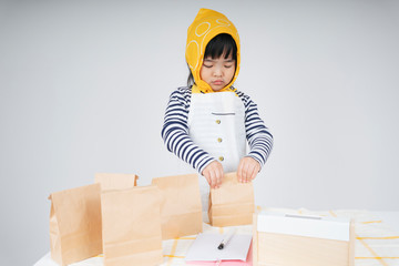 asian thai kid play role as a waitress wearing yellow bandage packing food in paper bag.