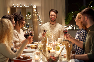 Wall Mural - holidays, celebration and people concept - happy friends having christmas dinner party drinking non-alcoholic red wine at home