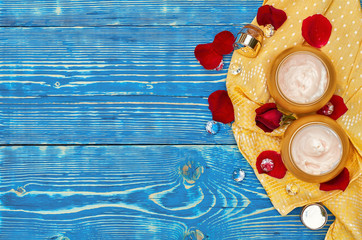 round jars of cosmetic cream. Cosmetic mock up bottles. Flat lay top view copy space. Natural skincare beauty product concept. on a blue wooden background and an orange napkin and red rose petals