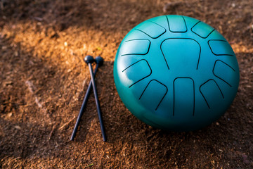 Close-up of a hand pan steel tongue drum musical instrument and a pair of black drum sticks on the brown background of the earth. Relaxing and healing sounds, music therapy. Copy space.