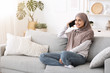 © Prostock-studio - Happy arabic woman talking on cellphone while sitting on couch at home
