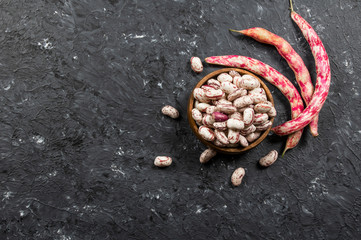 Harvested uncooked dried roman beans with raw pod plant on rustic background, heap of legume kidney bean concept