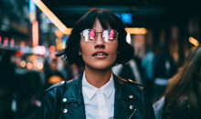 Caucasian Woman In Optical Spectacles With Neon Reflection Of Lights Standing At Urbanity During Travel Vacations For Visiting New York, Attractive Hipster Girl In Trendy Apparel Going Out