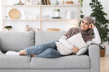 Canvas Print - Relaxed arabic woman lying on couch at home, cuddling pillow, enjoying weekend