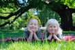 two little girls in wreaths of dandelions lying on the grass