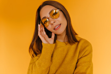 Wall Mural - Spectacular female model in sparkle glasses standing on yellow background. Sensual white girl in sweater posing with interest.