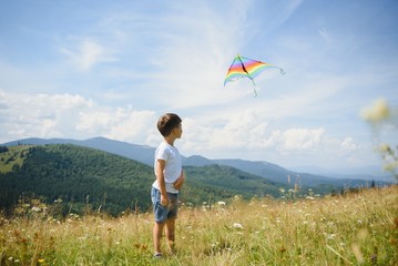 little boy holds string of kite flying in blue sky with clouds in summer with copyspace