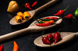 © BY BRAZIL - Various types of peppers in wooden spoons on a black background. Top view.
