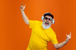 Crazy dance. Portrait of senior hipster man using devices, gadgets isolated on orange studio background. Tech and joyful elderly lifestyle concept. Trendy colors, forever youth. Copyspace for your ad.