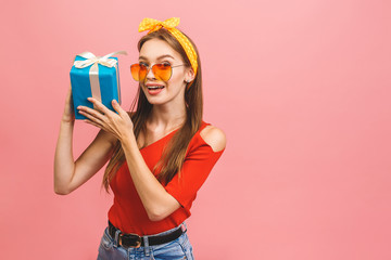 Wall Mural - Smiling young beautiful woman holds gift box. Isolated over pink background. Studio shot.