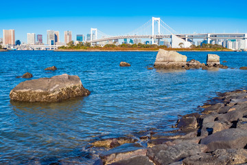 Wall Mural - Japan. Rainbow bridge in Tokyo. Suspension bridge over Tokyo Bay. The bridge leads to the island of Odaiba. Travel to the artificial Islands of Tokyo. Rocks and blue water of the Bay.