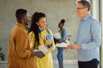 Canvas Print - Happy university teacher talking to his students in a hallway.