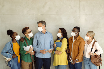 Canvas Print - Group of university students and their professor wearing protective face masks while talking against the wall.