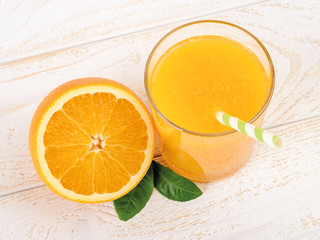 Glass of freshly squeezed orange juice and half of ripe sweet orange on a white wooden table. Vegetarian, raw food diet and healthy eating. Close-up.