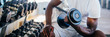 © twinsterphoto - Young African American man sitting and lifting a dumbbell close to the rack at gym. Male weight training person doing a biceps curl in fitness center