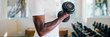 © twinsterphoto - Young African American man standing and lifting a dumbbell with the rack at gym. Male weight training person doing a biceps curl in fitness center