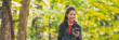 Autumn walk in the forest banner. Asian woman texting using mobile phone on outdoor hike walking in nature trail path panoramic background. Happy girl holding cellphone on active leisure activity.
