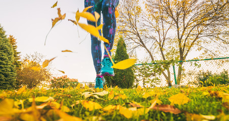 Wall Mural - Autumn foliage running woman in yellow leaves. Runner training outside in nature park in fall. Closeup of legs and shoes.