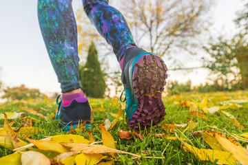 Wall Mural - Autumn run sport outside. Running woman in yellow leaves. Runner training in fall foliage nature park. Closeup of legs and shoes.