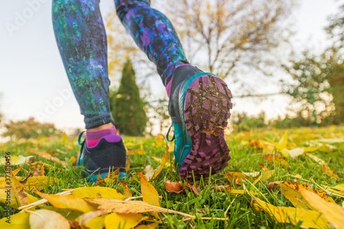 Autumn run sport outside. Running woman in yellow leaves. Runner training in fall foliage nature park. Closeup of legs and shoes.