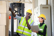 © Akarawut - African American and Asian workers wearing safety vest while working in warehouse checking for the inventory of product using laptop
