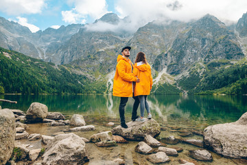 Wall Mural - man with woman in yellow raincoat at sunny autumn day looking at lake in tatra mountains