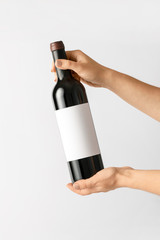 Hands holding bottle of wine with blank label on light background. Mockup for design