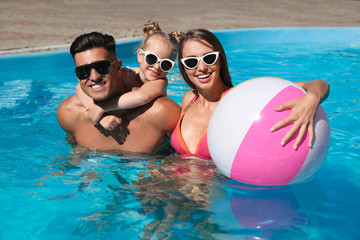 Wall Mural - Happy family with inflatable ball in outdoor swimming pool on sunny summer day