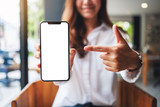 Fototapeta  - Mockup image of a beautiful woman pointing finger at a mobile phone with blank white screen