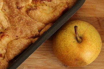 Homemade apple pie in a baking sheet and a juicy pear on a wooden table. Charlotte pie. View from above.