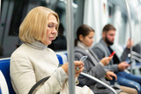 Fototapeta  - Focused woman browsing and typing messages on phone on way to work in modern metro car ..