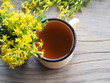 © Елена Захарова - Medical herb Hypericum with yellow flowers and herbal tea in an enameled mug on a wooden stand, top view. Useful plant Hypericum perforatumfor use in alternative medicine