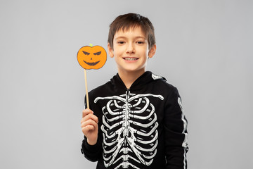 Wall Mural - halloween, holiday and childhood concept - smiling boy in black costume of skeleton with jack-o-lantern pumpkin party prop over grey background