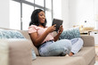 © Syda Productions - people, technology and leisure concept - happy young african american woman sitting on sofa with tablet pc computer at home