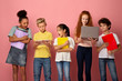 © Prostock-studio - Portrait of multiethnic schoolchildren with notebooks using tablet and laptop to study on pink background
