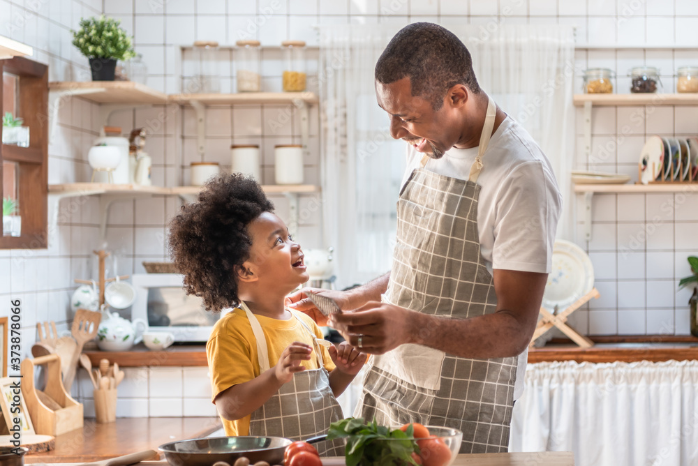 African American Father and son laughing while cooking in kitchen - obrazy, fototapety, plakaty 