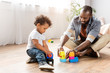 Young African American man playing with building blocks on floor with little son