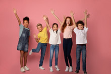 Cheerful Multiethnic Schoolkids Lifting Their Hands Up On Pink Background