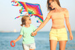 © Pixel-Shot - Woman and her little daughter flying kite on sea beach at resort